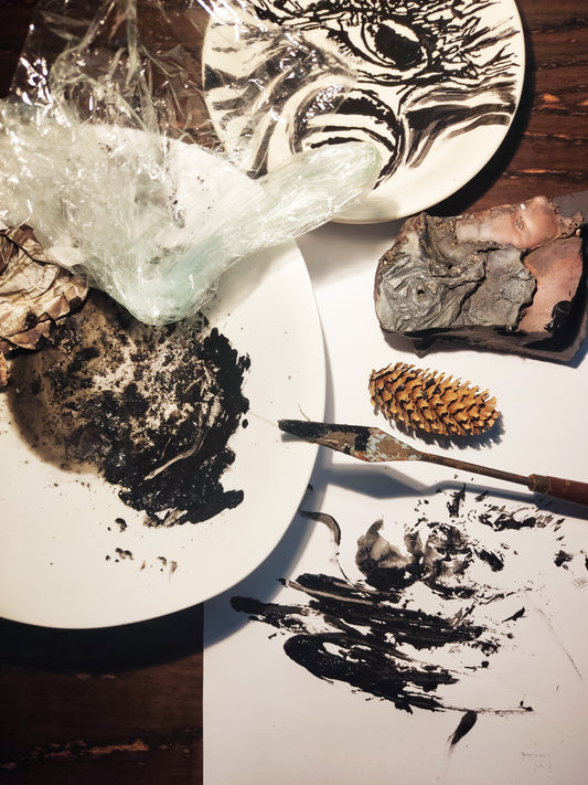 Dark art texture experiment by Emily Yap Design featuring black acrylic paint, a palette knife, charred paper, and volcanic rock on a cracked white plate.