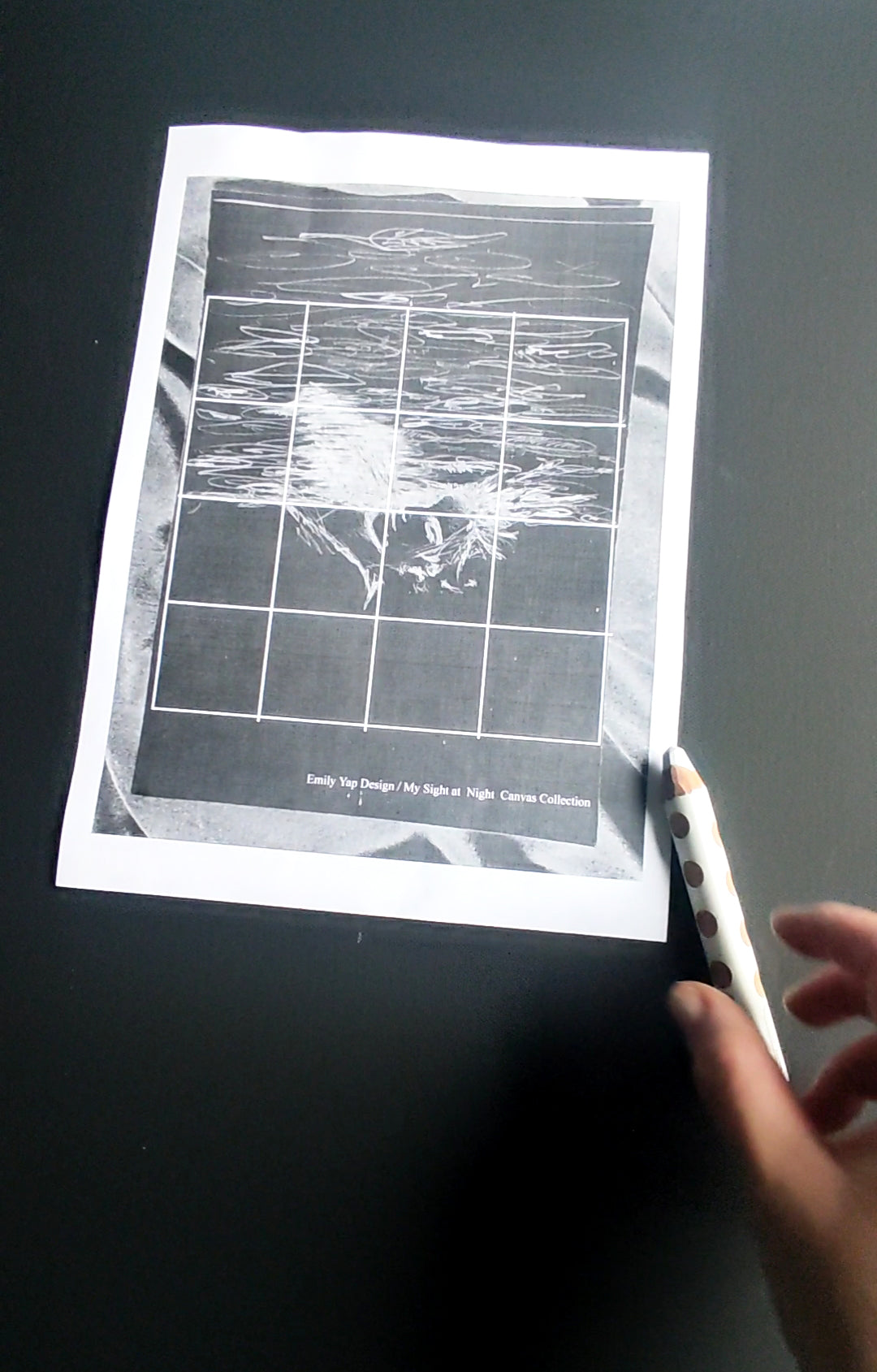 Artist hands drawing white grid lines on a black canvas with a printed draft blueprint by a window light