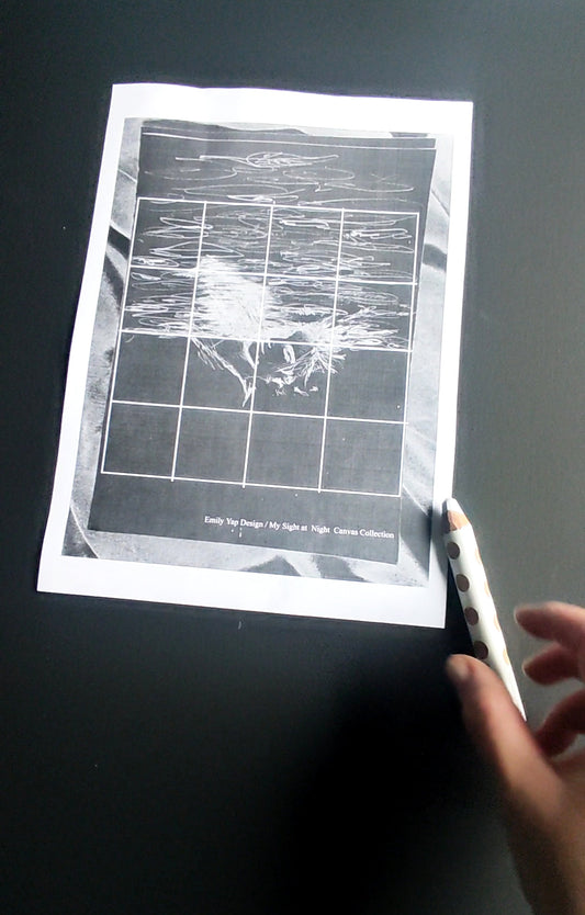 Artist hands drawing white grid lines on a black canvas with a printed draft blueprint by a window light